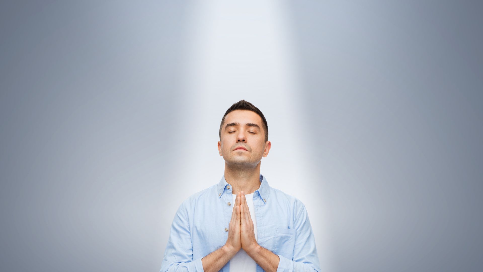 Homem com blusa branca e as mãos unidas na frente do corpo fazendo um gesto de oração para acalmar o coração.