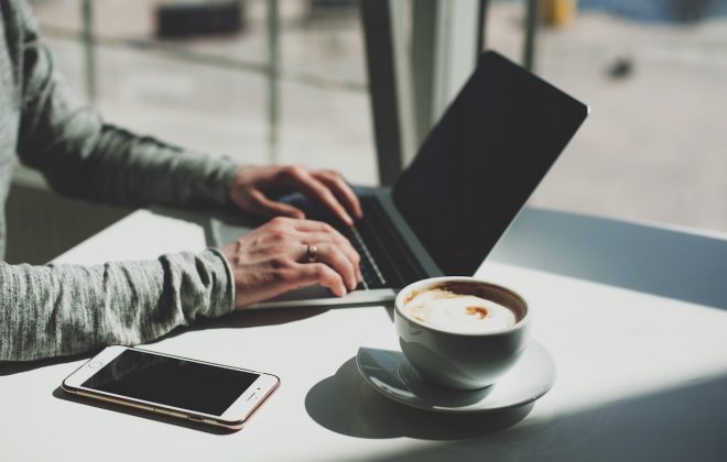 mãos de homem digitando em um laptop ao lado de uma xícara de café