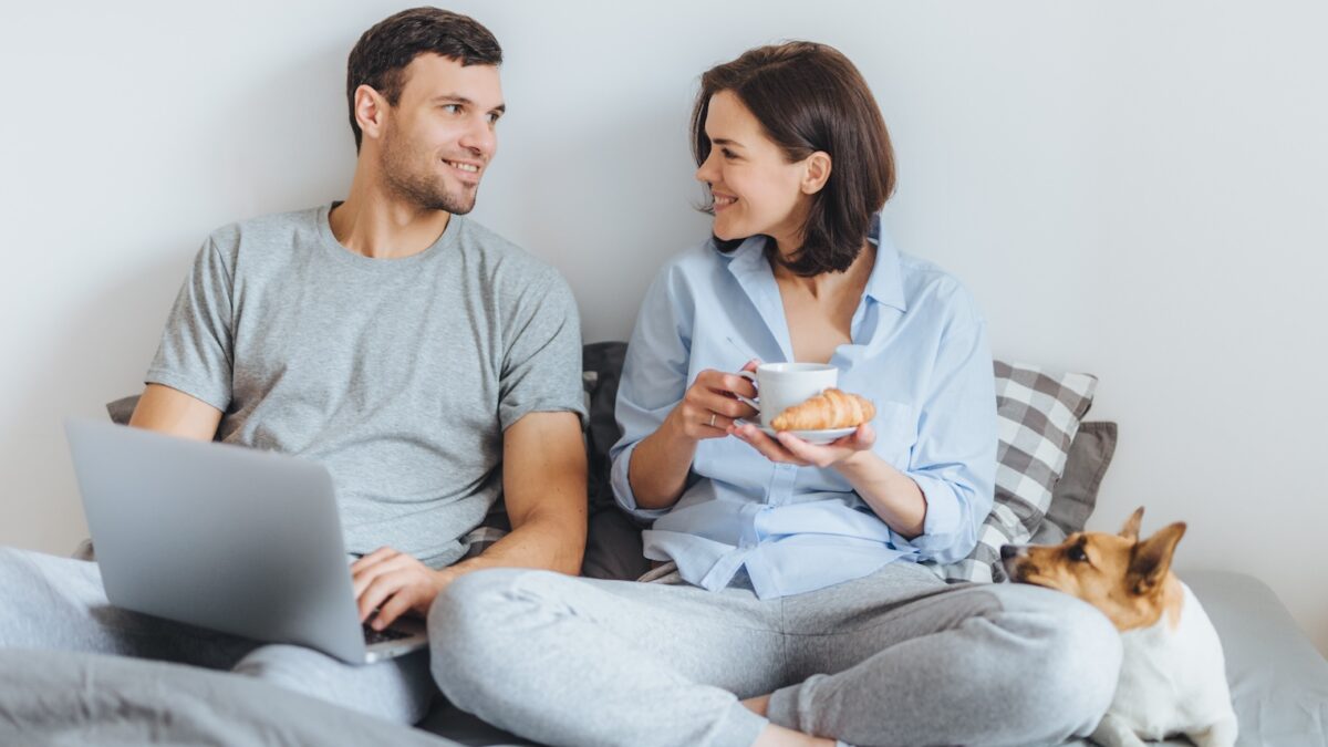 Casal se senta junto na cama, usa o laptop, tem uma conversa agradável entre si