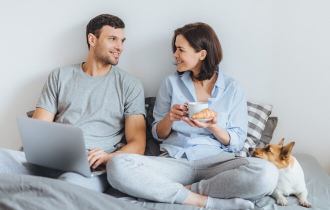 Casal se senta junto na cama, usa o laptop, tem uma conversa agradável entre si