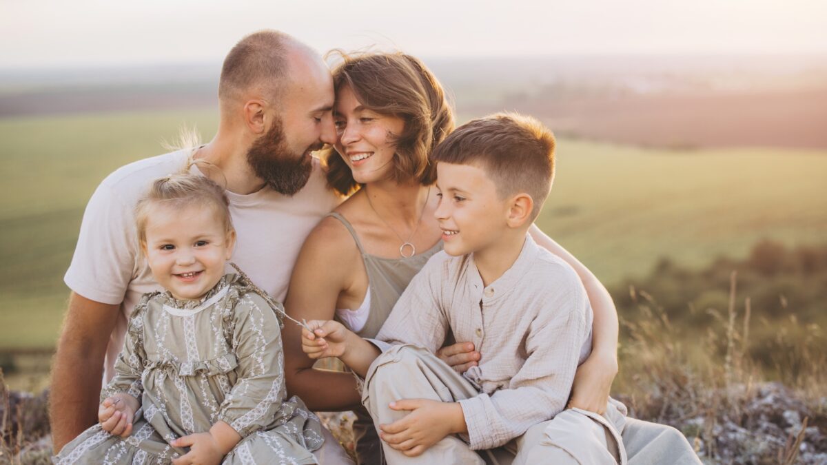 Família feliz aproveitando o tempo ao ar livre juntos, sorrindo e se abraçando em um campo panorâmico ao pôr do sol