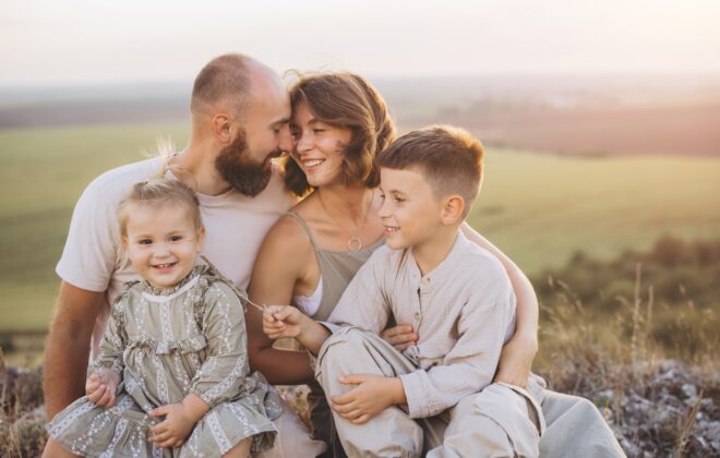 Família feliz aproveitando o tempo ao ar livre juntos, sorrindo e se abraçando em um campo panorâmico ao pôr do sol