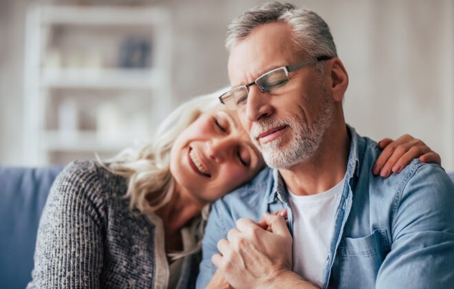 Love lives forever! Senior couple at home. Handsome old man and attractive old woman are spending time together. Sitting on a sofa, hugging and holding hands.